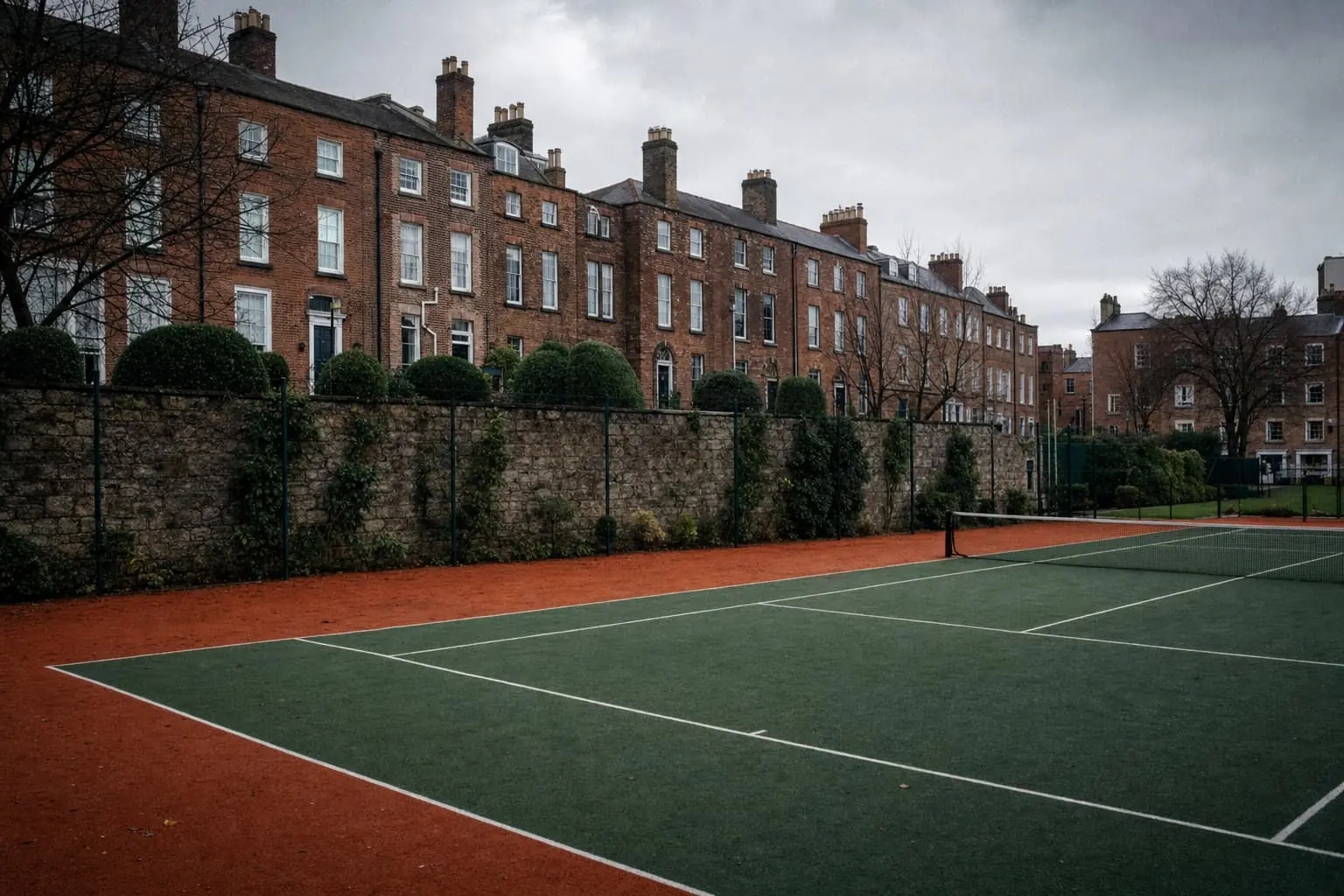 Club hard courts in Dublin under a bright grey sky, a granite wall and Georgian houses beyond.
