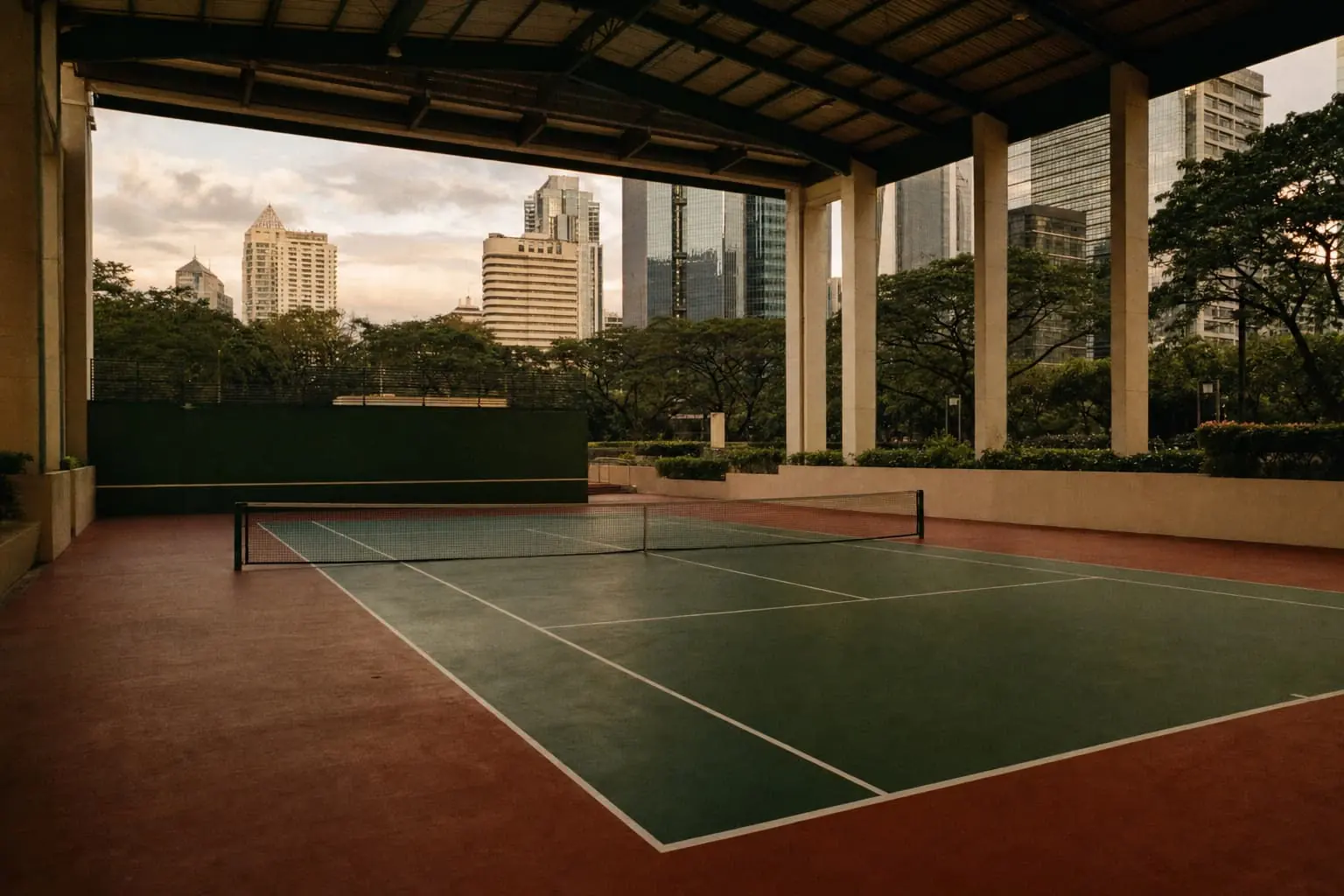 A covered hard court in Metro Manila open at the sides, acacia trees and glass office towers beyond the columns in evening light.