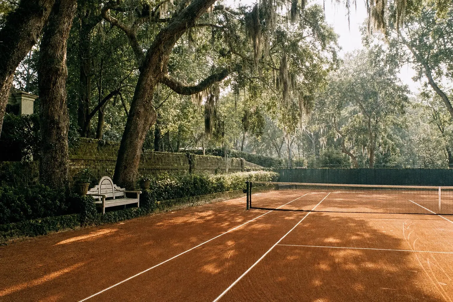 A clay court at a Wilmington club shaded by live oaks hung with Spanish moss, a white garden bench against an old brick wall.