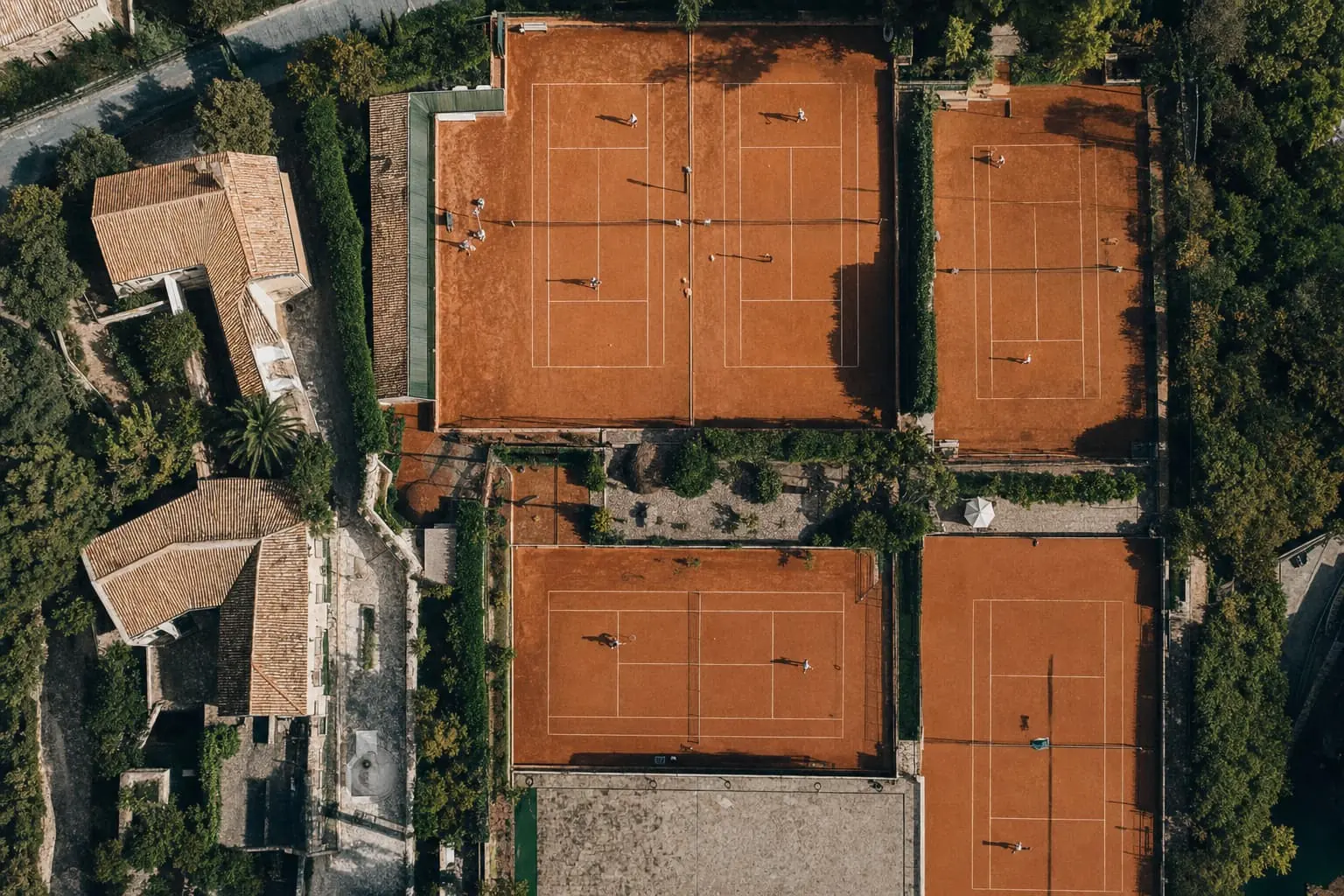 Aerial view of clay tennis courts spread between rooftops and trees
